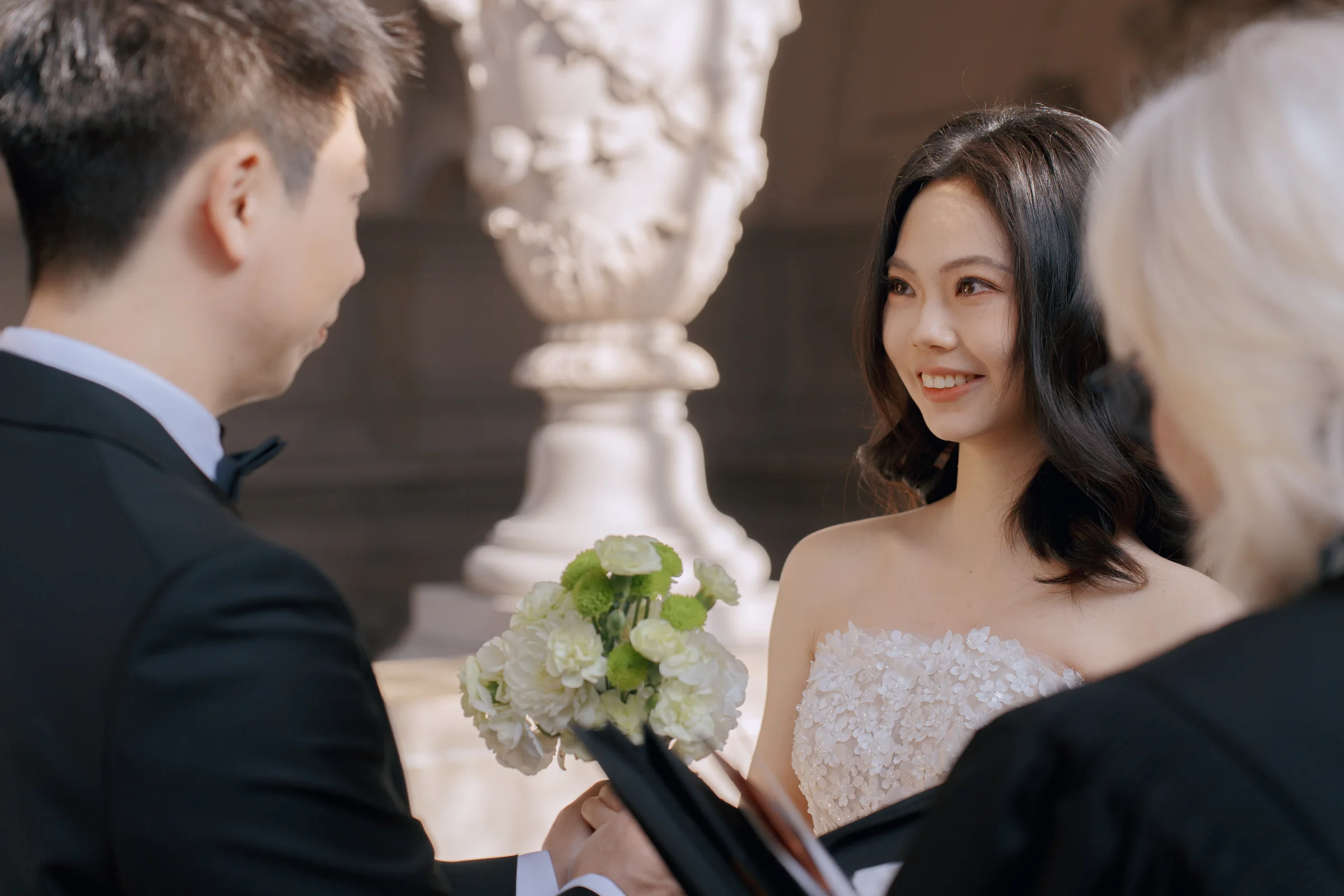 Bride smiling with her bouquet as the officiant speaks during the ceremony