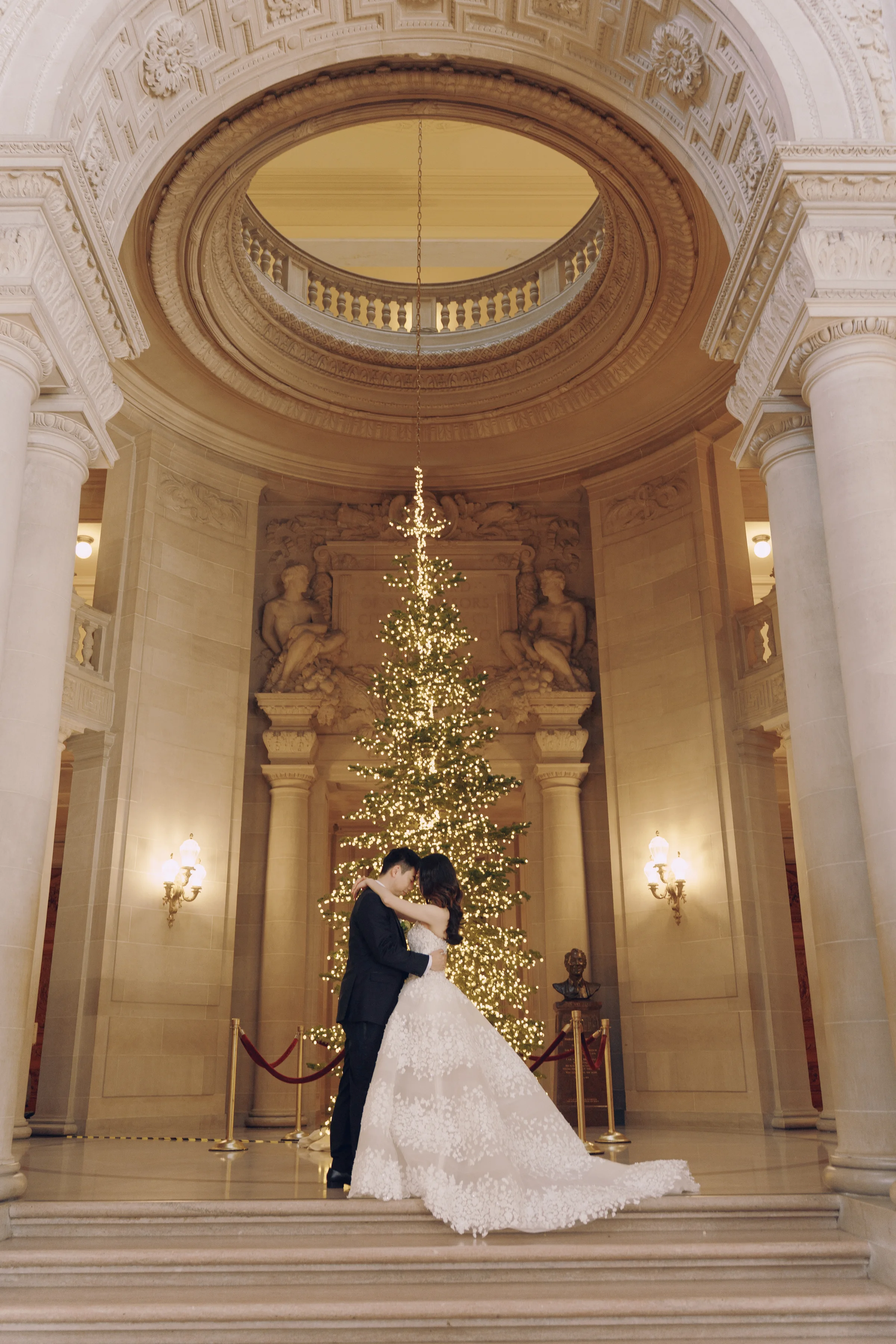 Couple embracing before the lit Christmas tree under the grand rotunda arch