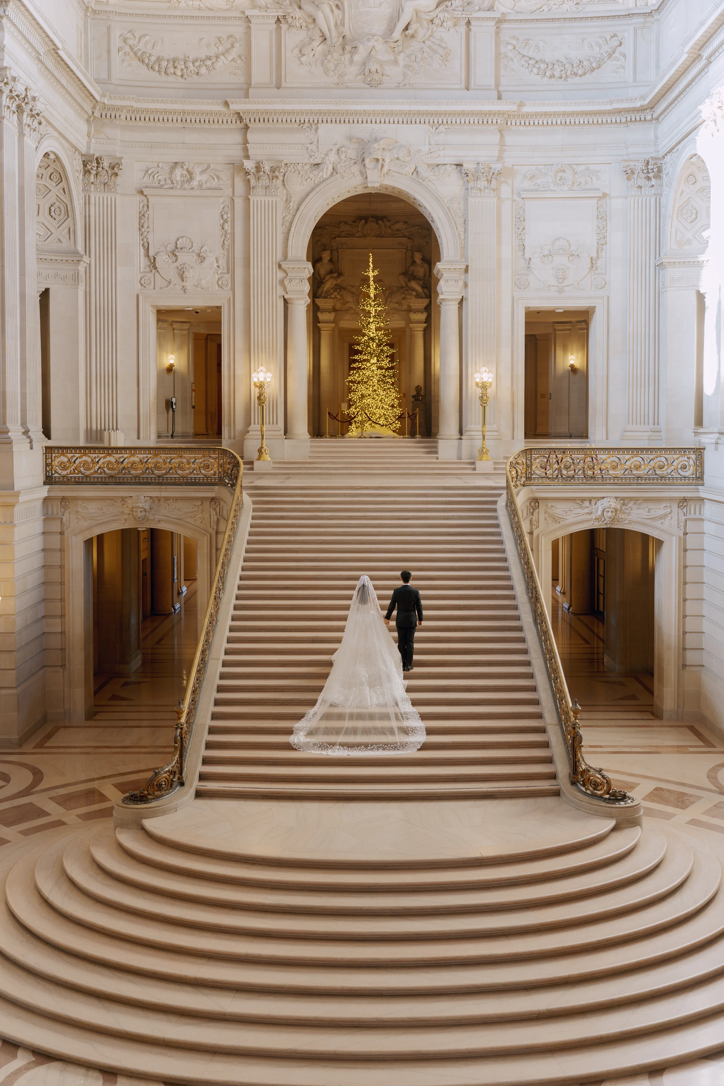 Groom leading the bride down the grand staircase in a wide architectural view