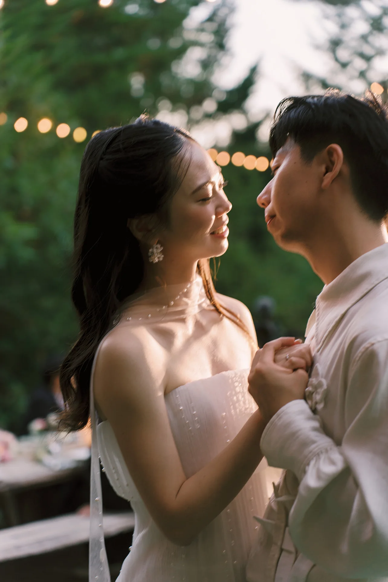 Newlyweds holding hands beneath string lights in the redwood garden at Sparrow Valley Retreat.