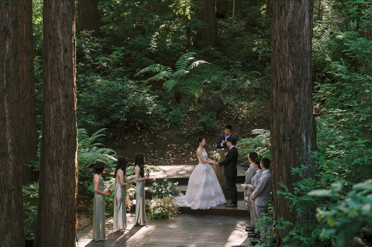 Newlyweds exchanging vows on a woodland platform with attendants standing on either side.