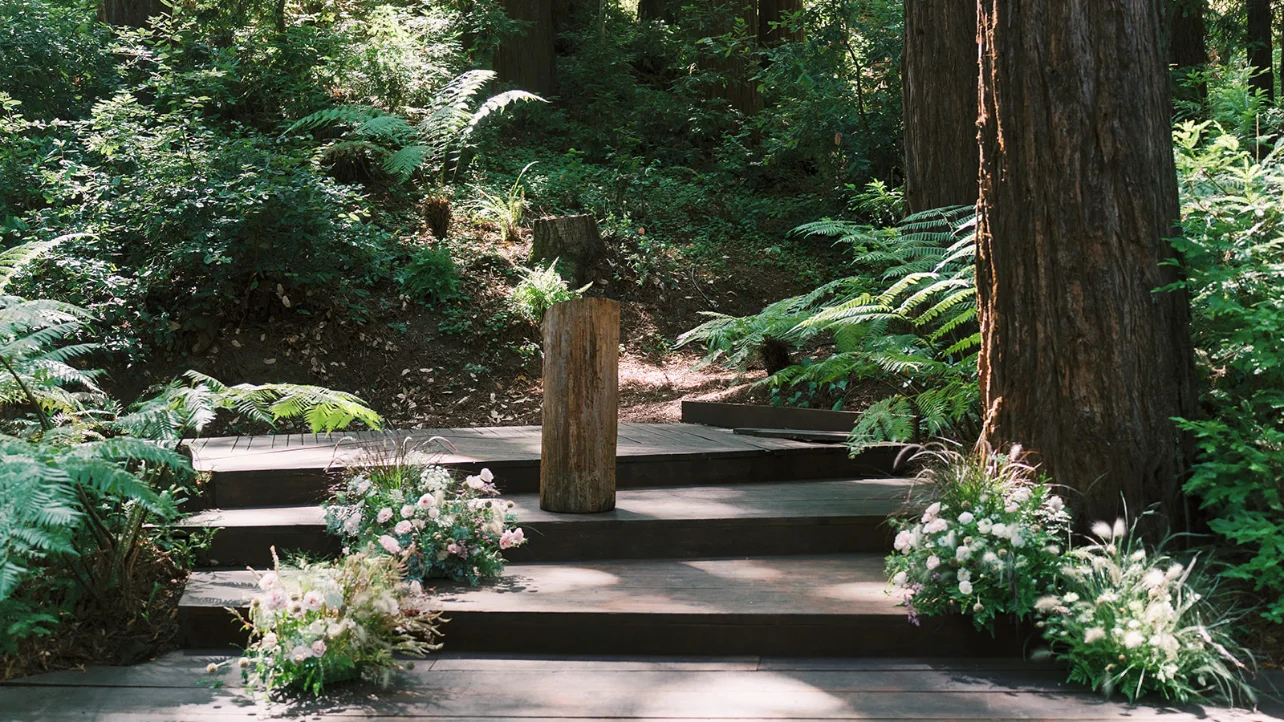 Redwood forest ceremony aisle lined with loose pink-and-white floral arrangements