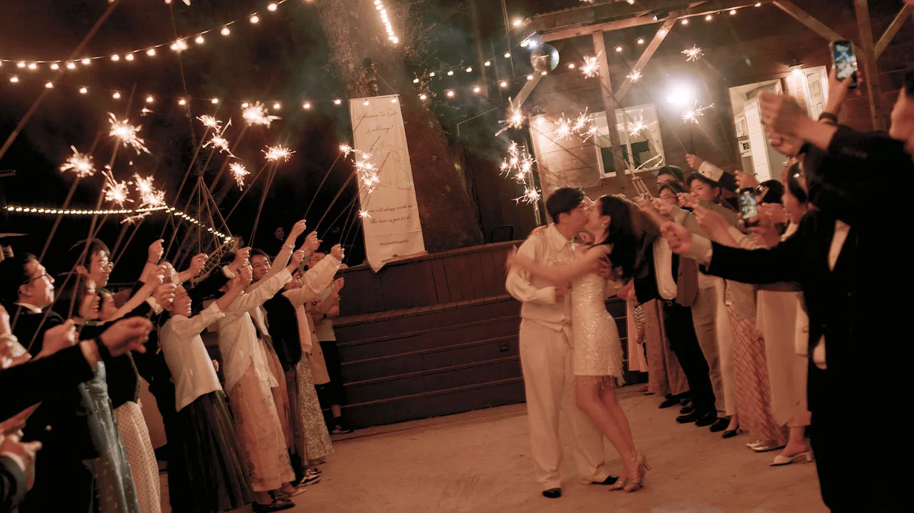 Newlyweds kissing beneath string lights during a nighttime sparkler exit