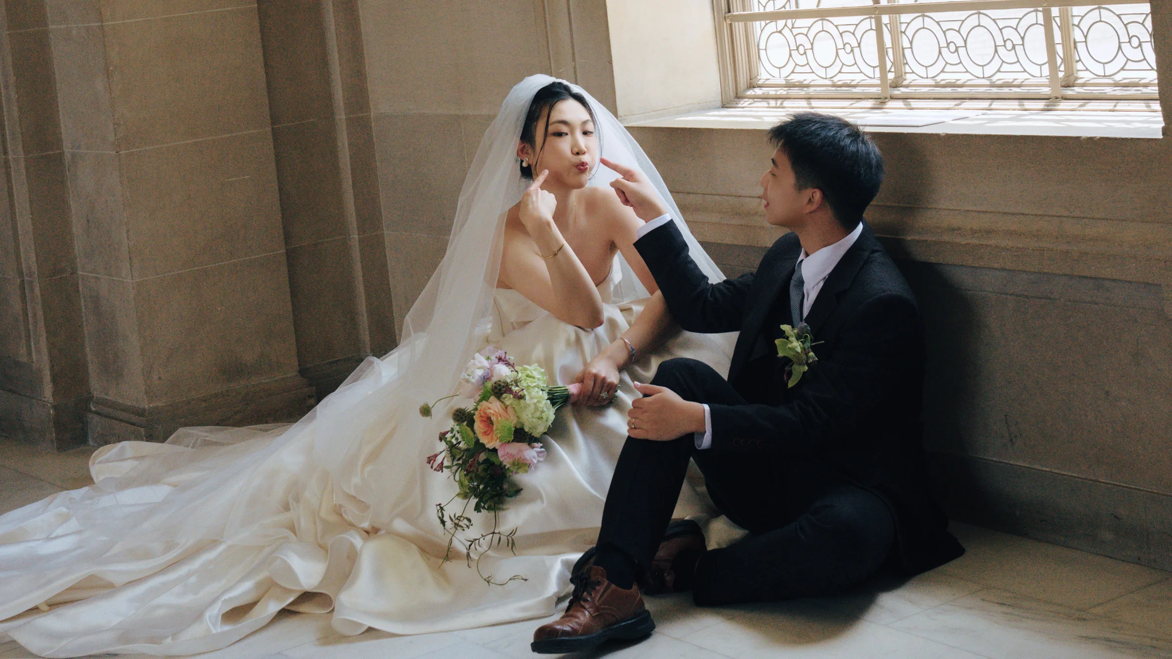 Groom gently adjusting the bride's veil as they sit together in an ornate interior