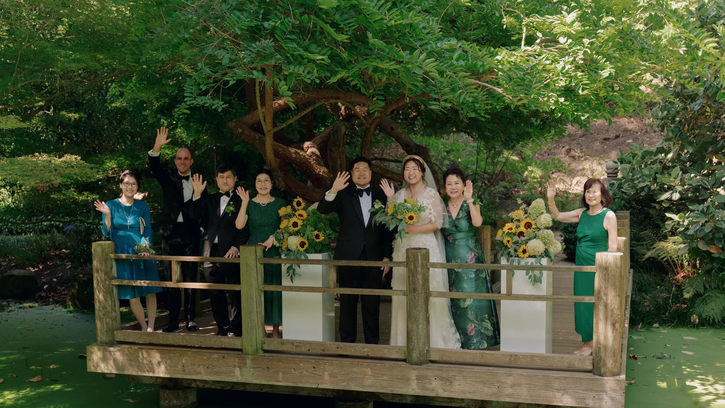 Wedding party waving from a wooden bridge surrounded by a lush garden