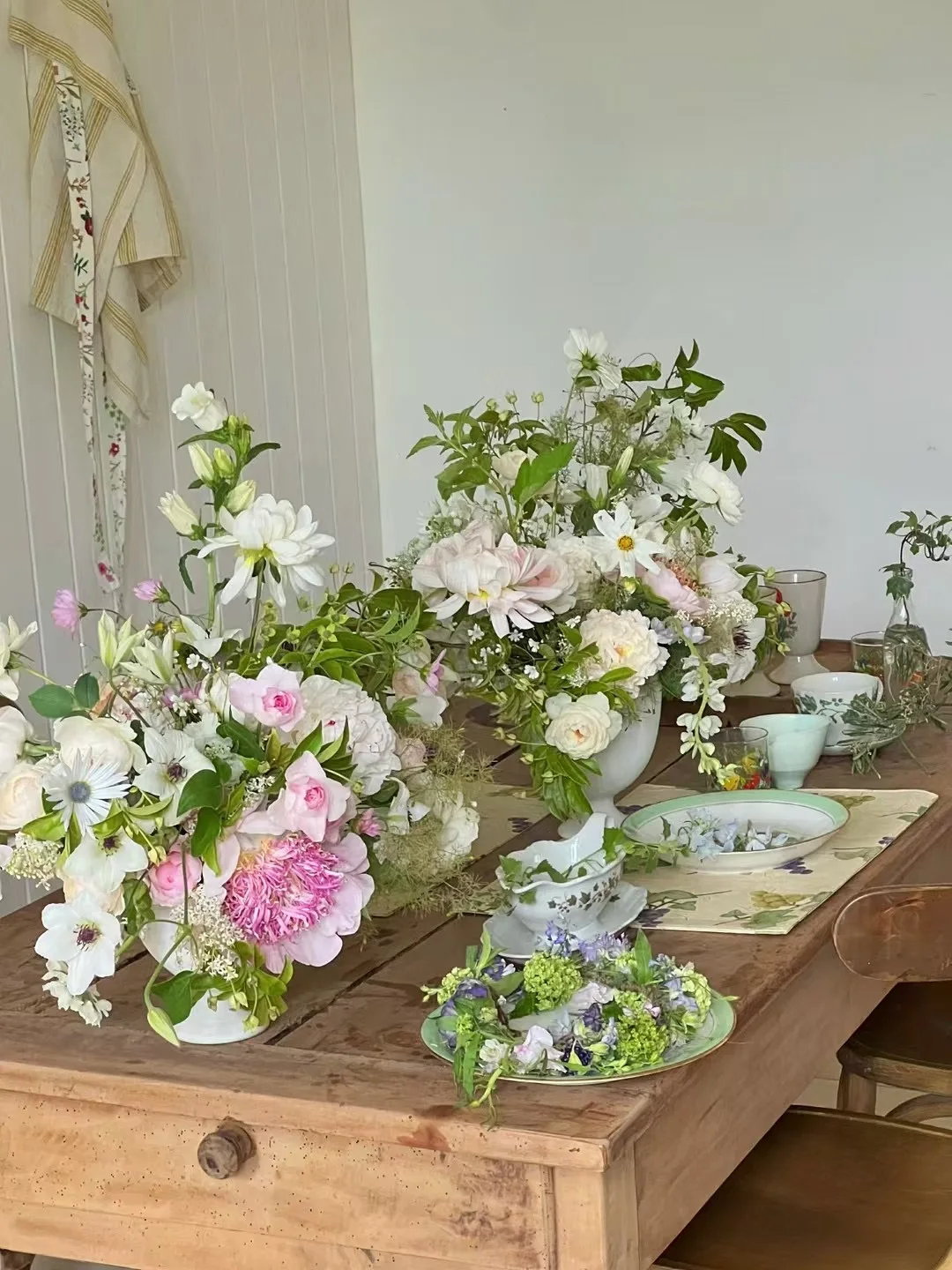 Cluster of pastel garden arrangements in white footed vases on a rustic wooden table